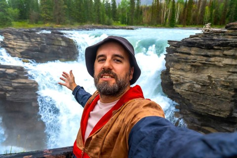 Happy tourist taking a selfie with powerful athabasca falls cascading into a narrow gorge in the