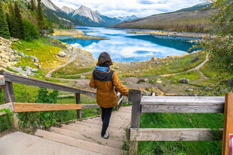 Female tourist walking down wooden stairs to medicine lake, with turquoise waters reflecting