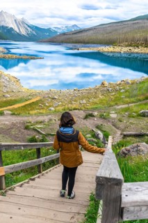 Female tourist walking down wooden stairs approaching medicine lake with turquoise water reflecting