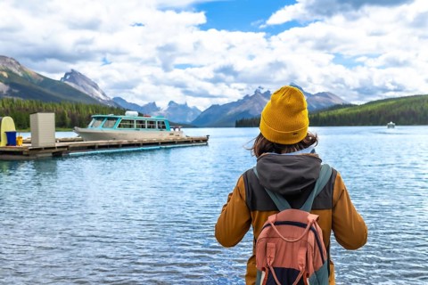 Female tourist wearing a yellow beanie and carrying a backpack admires the stunning view of maligne