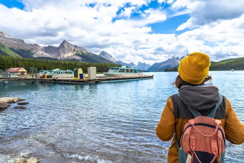 Female tourist wearing a yellow beanie and carrying a backpack admires the stunning landscape of