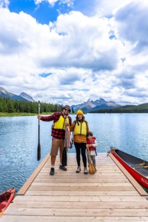 Family wearing life jackets standing on a wooden dock, ready for canoeing on maligne lake with the