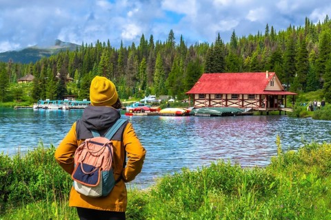 Female tourist wearing a yellow beanie and backpack admiring the iconic boathouse at maligne lake