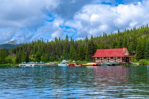 Colorful canoes and tour boats are docking at a boathouse with a red roof on maligne lake in jasper