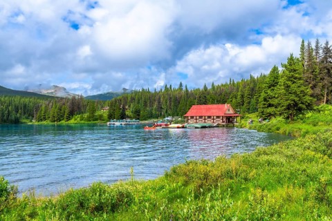 Beautiful summer landscape featuring a vibrant red roofed boathouse on the serene shores of maligne