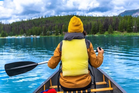 Tourist wearing yellow life jacket and beanie paddling a canoe in maligne lake, jasper national