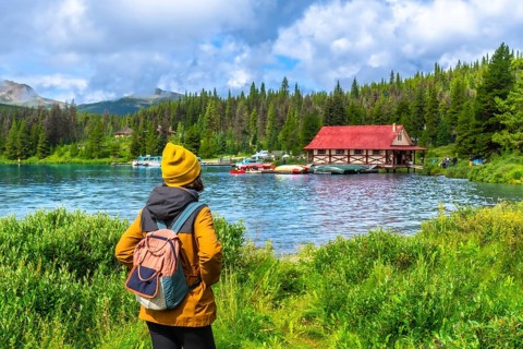 Female tourist wearing a yellow beanie and backpack enjoying the breathtaking view of maligne lake