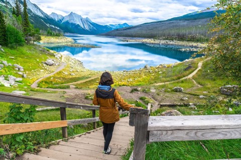 Female hiker descending wooden stairs towards the scenic medicine lake, surrounded by the canadian