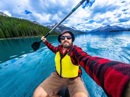 Tourist wearing sunglasses and life jacket kayaking and taking a selfie in maligne lake with