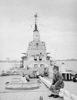 Boy sitting on deck of Royal Navy HMS Vanguard battleship, Devonport, Plymouth, Devon, England, UK