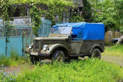 Old off-road vehicle with blue tarpaulin cover standing in overgrown green surroundings, Soviet