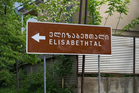 Brown road sign points towards Elisabeththal in Georgian and English letters, village founded by