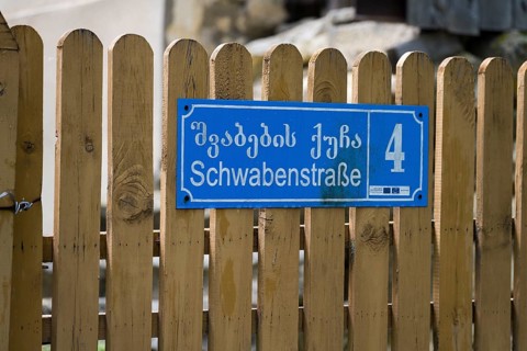 Blue street sign with house number 4 on a wooden fence in Georgian and German letters,