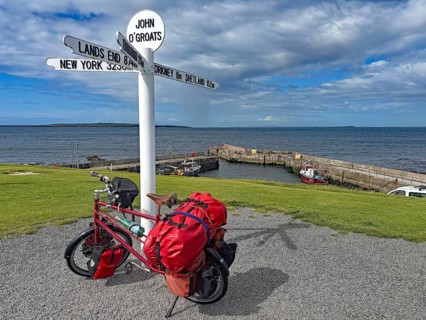 Packed bike in front of lake sign and harbor view in John O'Groats, bicycle trips, bicycle