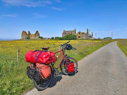 Bicycle with luggage on a dirt road in front of ruins amidst blooming countryside, South Uist,