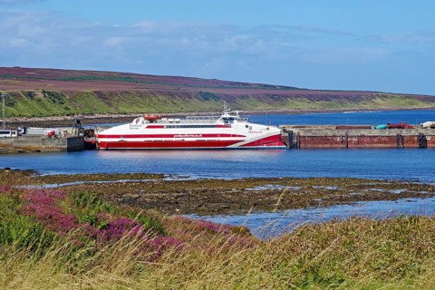 Ferry in harbour in front of a quiet coastal landscape with purple heath, catamaran, ferry to St.