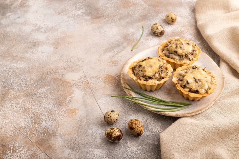 Tartlets with meat and cheese on brown concrete background and linen textile. side view, copy space