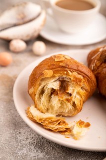 Croissant on white plate on brown concrete background and linen textile, cup of coffee, side view,