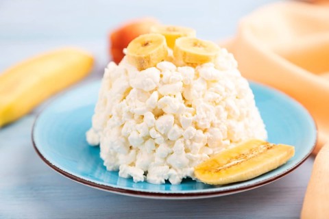 White ?ottage cheese, Curd, with Banana on blue wooden background and orange textile, side view,