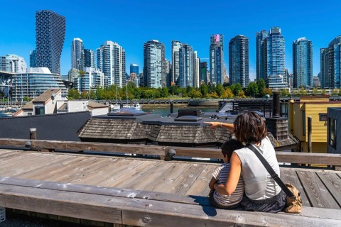 Mother and son sitting on a wooden boardwalk, pointing towards the stunning vancouver skyline from