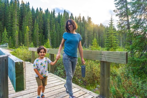 Mother and son holding hands, smiling and walking on a wooden boardwalk surrounded by lush green