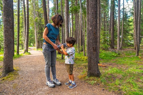 Mother giving a drink of water to her son from a reusable water bottle while hiking on a beautiful