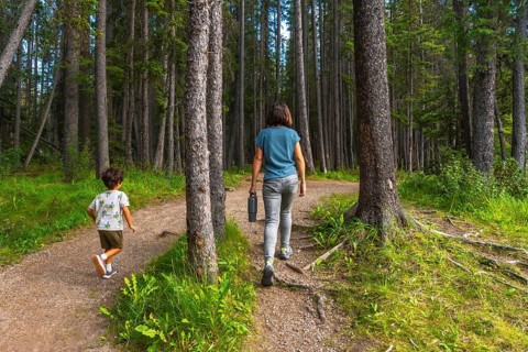 Mother carrying a water bottle and her son enjoying a leisurely hike along a picturesque forest
