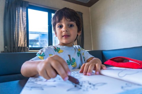 Young boy concentrating on drawing with crayons in a camper van, enjoying creative activities