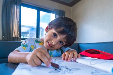 Young boy enjoys a creative moment, drawing with crayons in a camper van, surrounded by the natural
