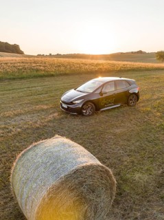 A black car is parked in a field next to a hay bale at sunset, deer e-car sharing, Cupra electric