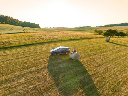 Car next to a hay bale in the middle of a vast golden field under the evening sun, deer e-car