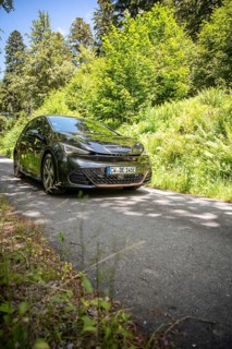 Car driving on narrow forest road surrounded by thick greenery and sunlight, Deer e-car sharing,