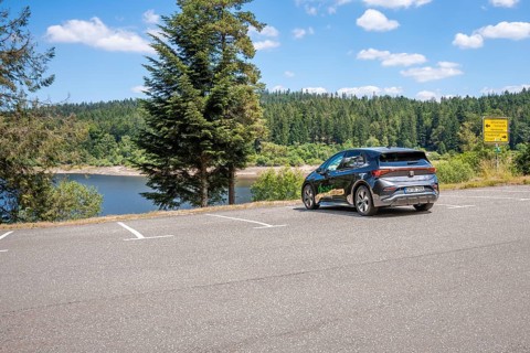 Car in a parking lot overlooking a lake and surrounded by a green forest, deer e-car sharing, Cupra