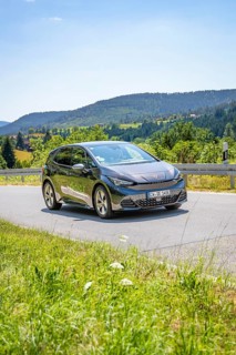 Black car driving on a road through a hilly landscape in daylight, deer e-car sharing, Cupra