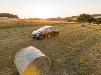 A car is parked in a field with hay bales at sunset, surrounded by meadows, deer e-car sharing,