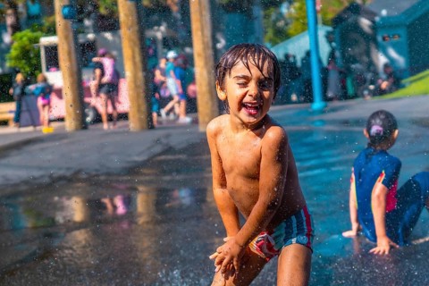 Cheerful child with wet hair and colorful swimming trunks laughing and playing in a city park