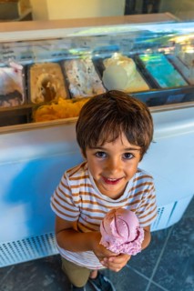 Smiling child holding a strawberry ice cream cone in front of a display case full of colorful ice