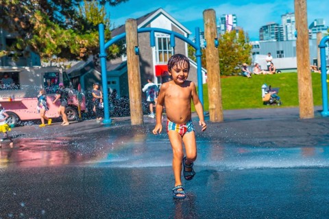 Happy child is running through water jets at a playground in vancouver, british columbia, on a