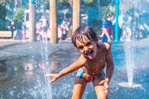 Happy child sticking out his tongue while playing in a water fountain on a sunny day in vancouver,