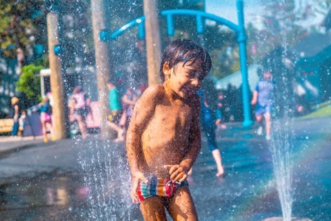Happy muddy child playing and enjoying a refreshing spray in a water fountain at a playground in
