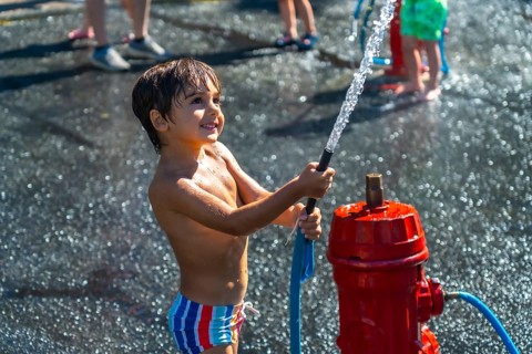 Smiling boy spraying water from a fire hydrant during a hot summer day in vancouver, british