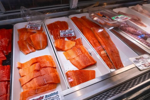 Fresh salmon fillets, cut into steaks and portions, are displayed on ice in a fish market in