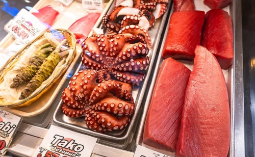 Fresh octopus and tuna fillets are displayed on ice alongside wasabi at a fish market in vancouver,