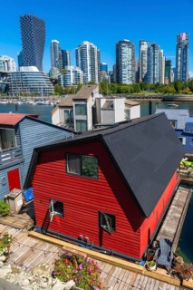Red floating house with open windows and potted flowers on the deck with other floating homes and