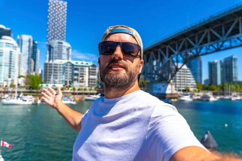 Happy man taking selfie with outstretched arm showing vancouver skyline, cambie street bridge and
