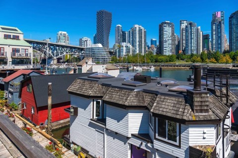 Colorful floating homes contrasting with vancouver's high rise skyline under a clear blue sky,