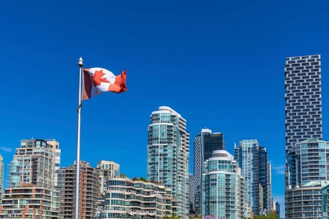 Canadian flag waving proudly in the foreground with the modern skyline of vancouver, british