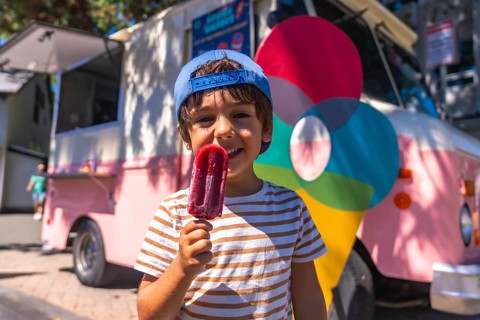 Smiling boy enjoying a refreshing popsicle on a sunny day, standing near a colorful food truck in