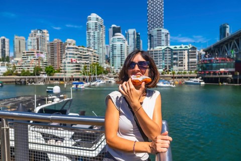 Young woman enjoying a delicious donut with the stunning cityscape of vancouver, british columbia,