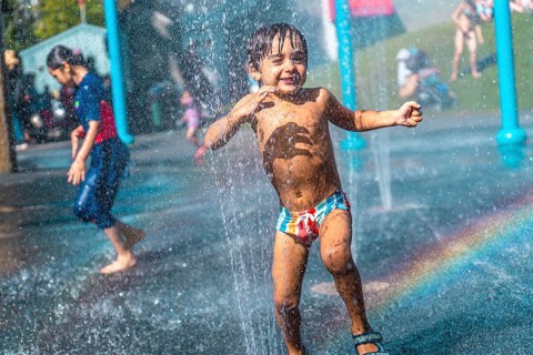 Happy child running through jets of water in a playful splash park on a hot summer day in